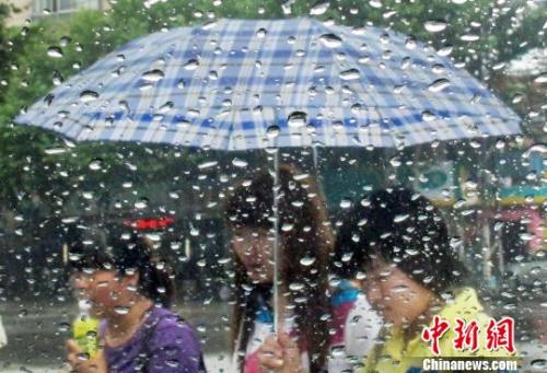 6月28日，隔着滴满雨珠的车窗，打着雨伞的市民在南京街头经过。泱波 摄